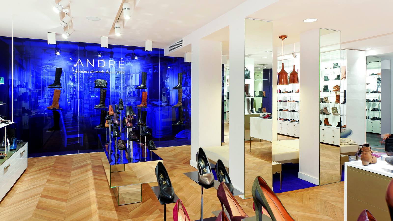 Intérieur d'un magasin de chaussures André avec un mur bleu portant le nom de l'enseigne, des bottes exposées et des escarpins au premier plan