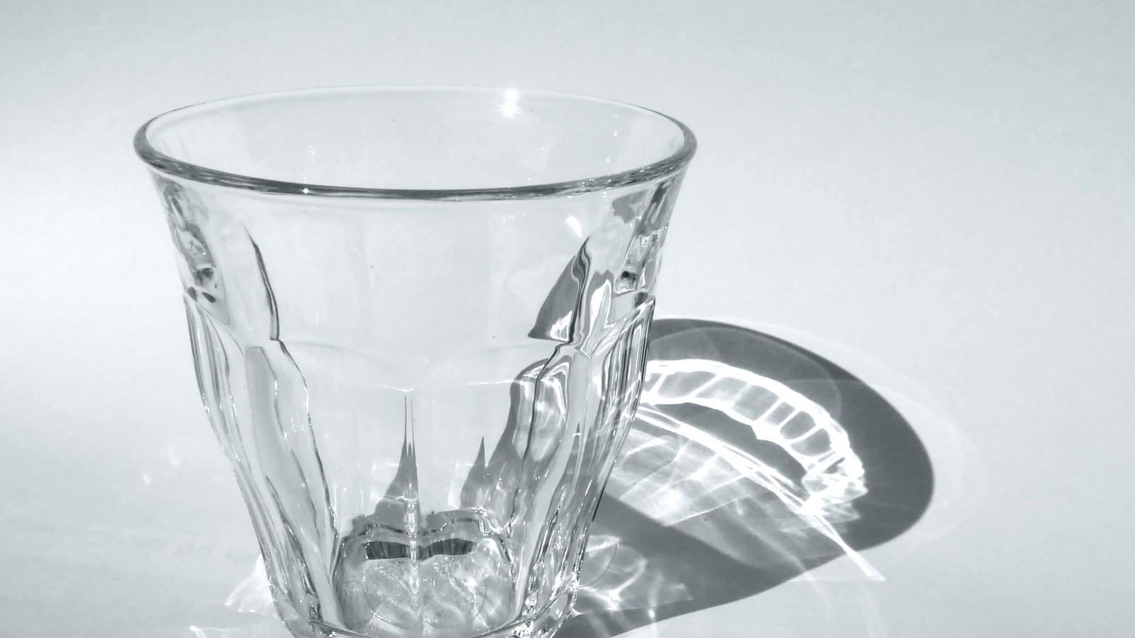 Un verre Duralex Picardie vide, posé sur une surface blanche, avec son ombre découpée par la lumière