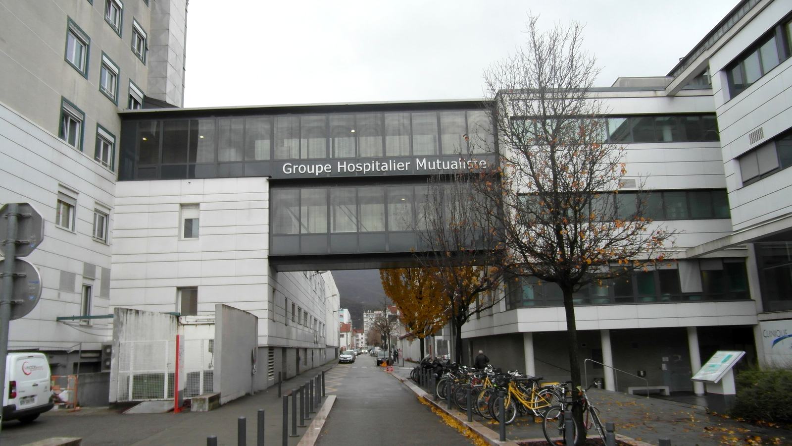Passerelle vitrée portant l'inscription Groupe Hospitalier Mutualiste au-dessus de la rue du Docteur-Hermitte à Grenoble, entre deux bâtiments de la clinique